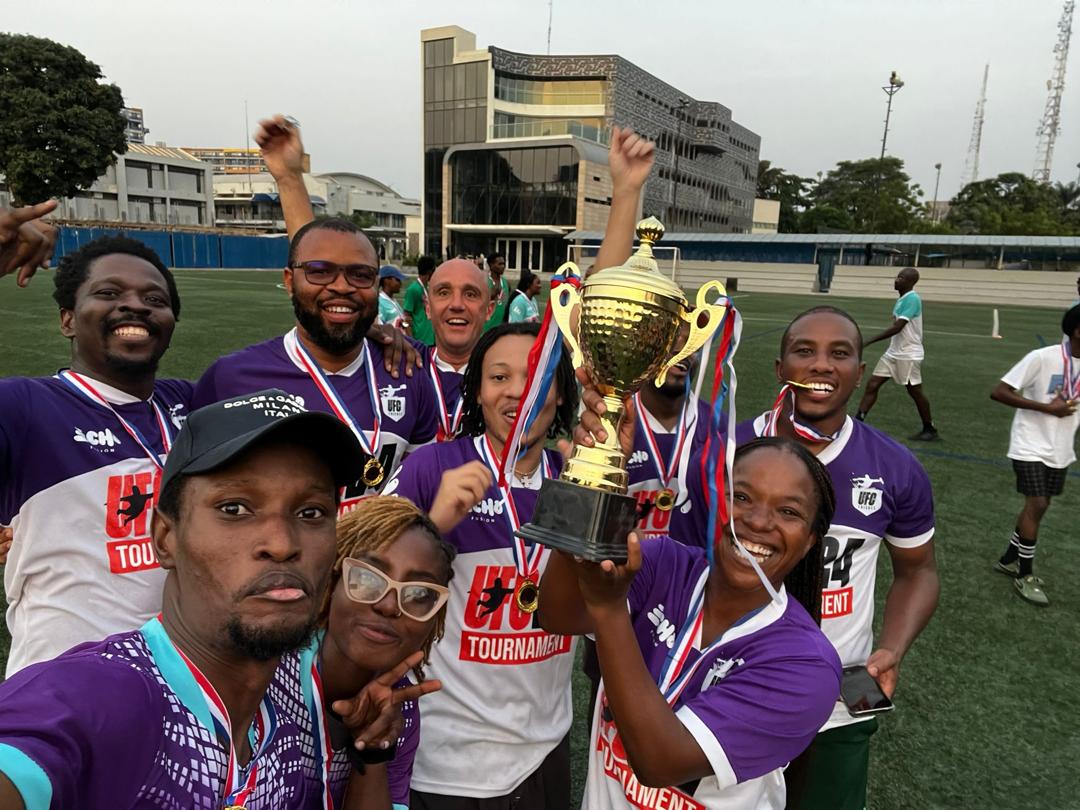 A sports team smiling together with medals and a trophy on the field